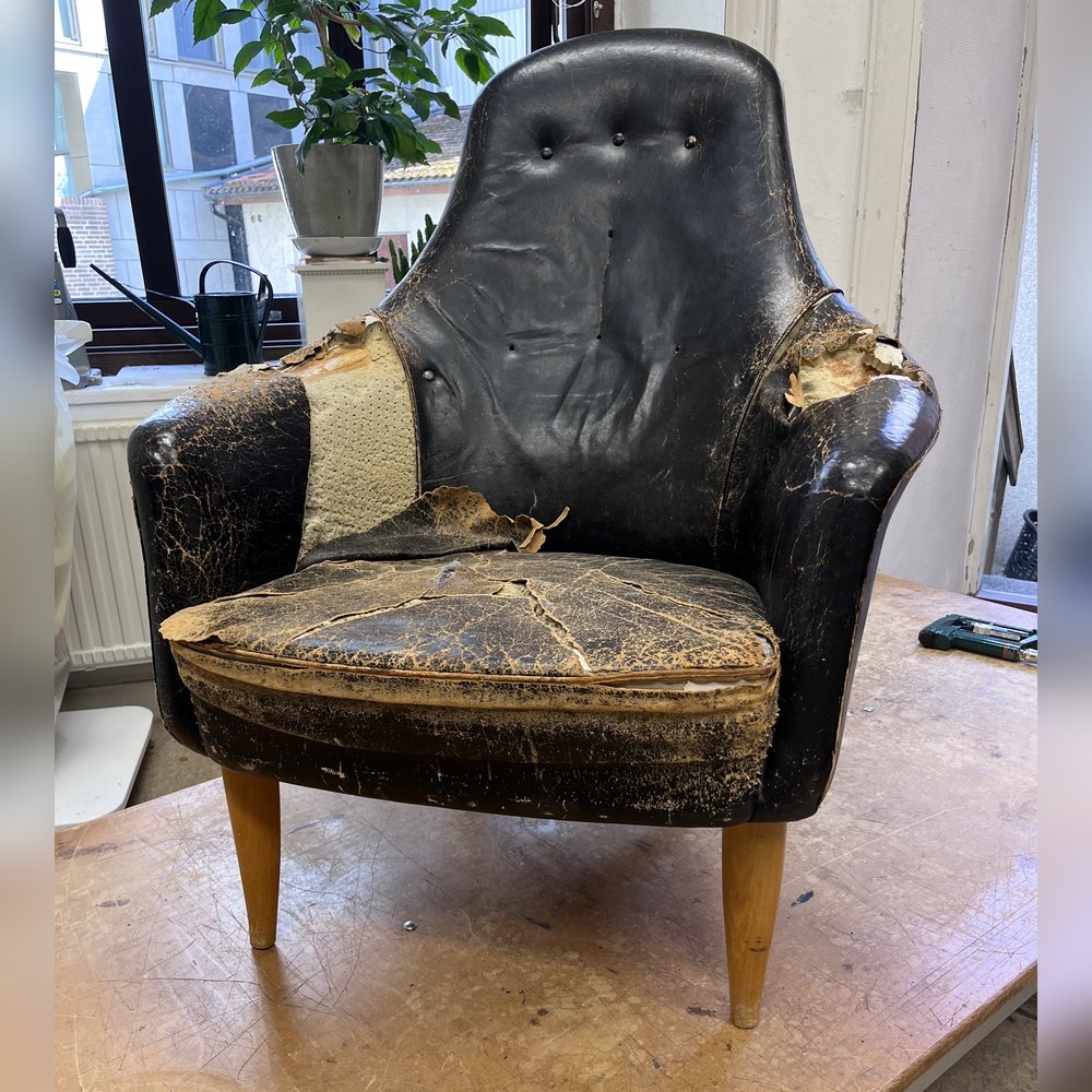 Fåtölj före omtapetsering, med slitet och sprucket svart skinn