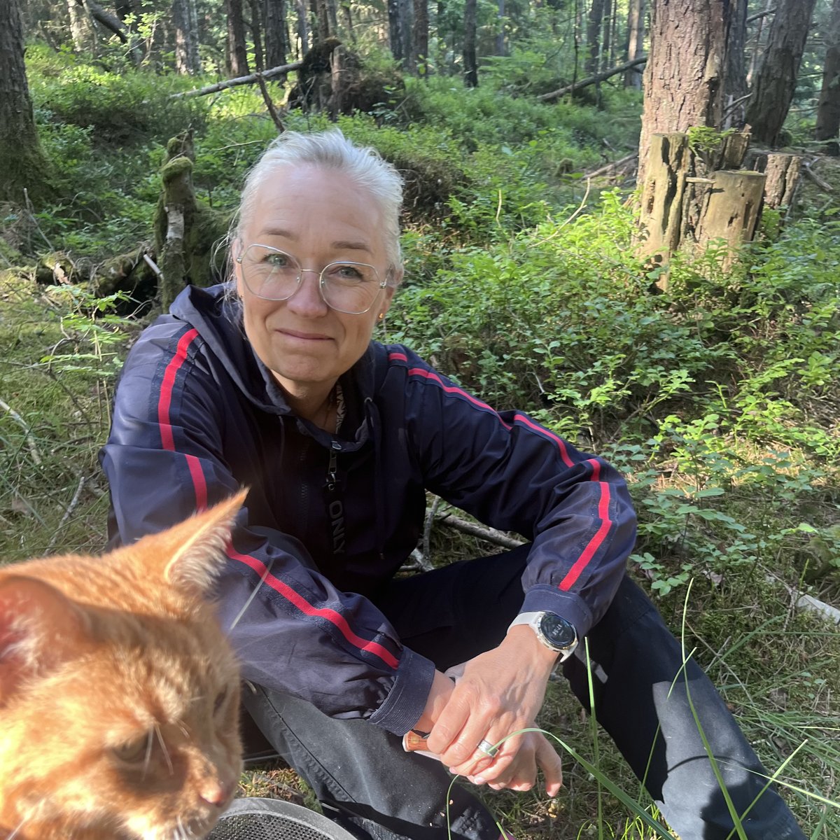 Amelie sitter i skogen tillsammans med en katt i förgrunden